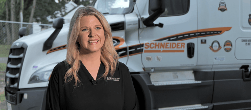 Schneider recruiter smiling, standing in front of Schneider semi truck