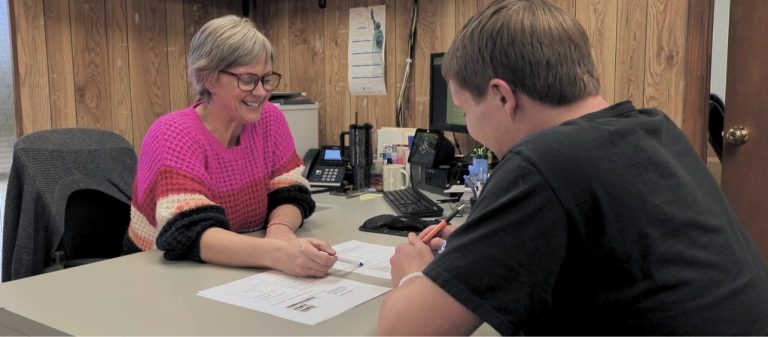 Admissions representative pointing at paper on a desk, across from a potential student