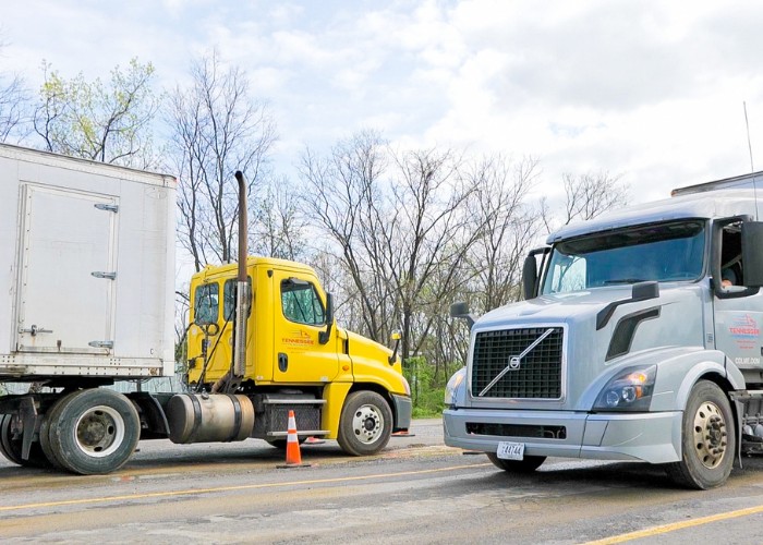 A yellow Tennessee CDL School and a gray semi-truck parked on a training lot with bare trees in the background