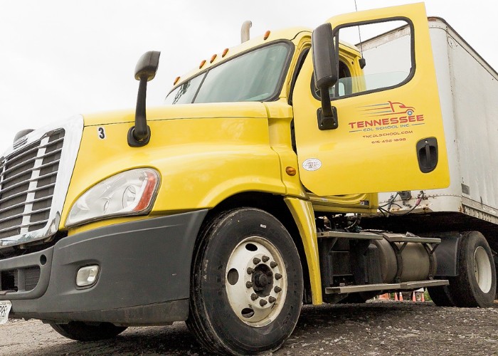 A yellow Tennessee CDL School semi-truck with a trailer and open cab door parked on a lot